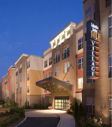 Preservation of Columbia Senior at MLK Village as shown in this evening view, a modern multi-story brick building with illuminated signage and a covered entrance.